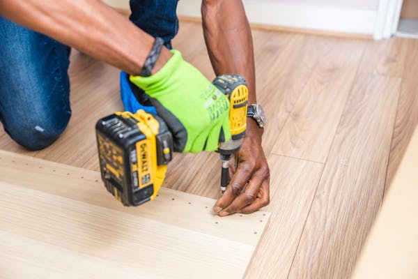 A man operates a drill while installing a wooden floor, demonstrating skilled craftsmanship in home improvement.